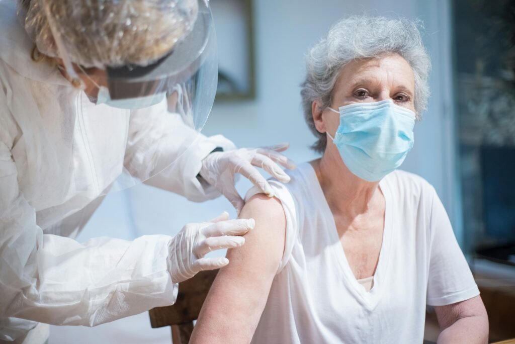 Senior woman wearing a mask getting vaccinated by a healthcare worker in PPE.